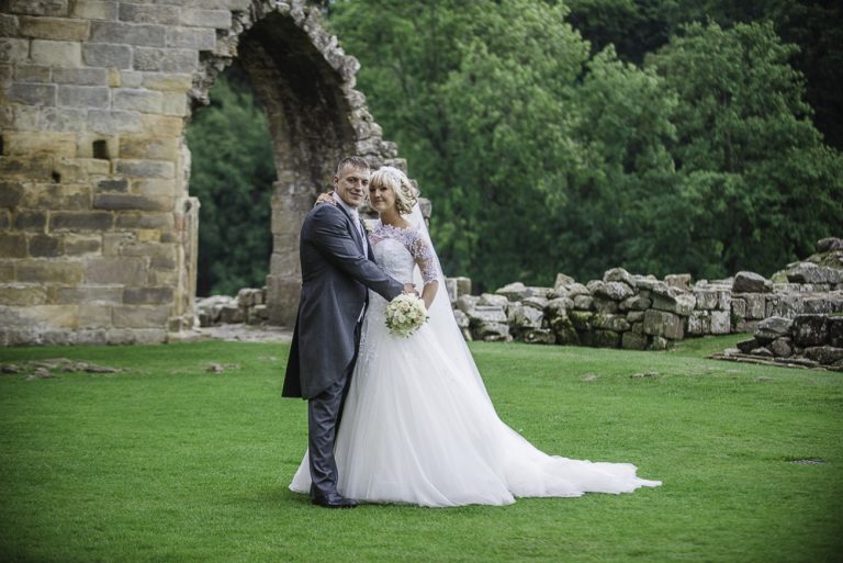 Bride and groom posing by ancient stone ruins and green landscape