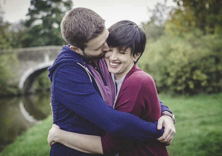 Couple embracing in a park with a bridge in the background