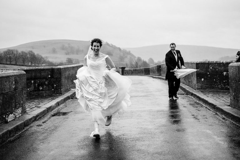 Bride and groom running joyfully on a rainy day bridge