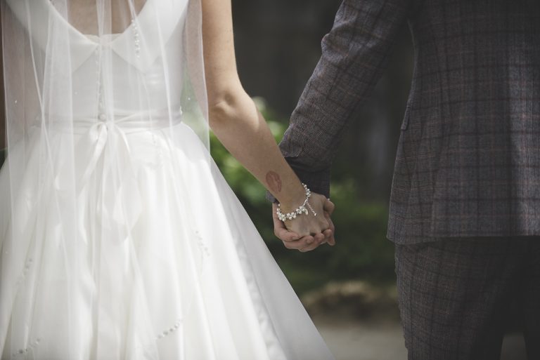 Bride and groom holding hands in wedding attire outdoors