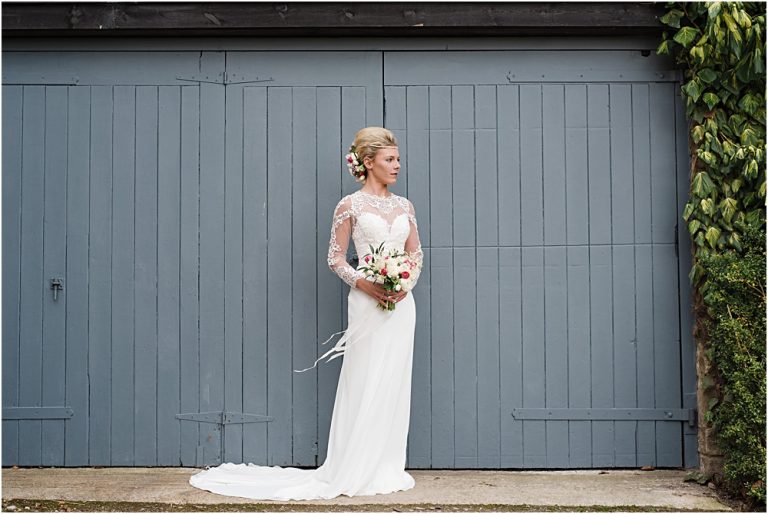 Bride in elegant gown holding bouquet by rustic blue doors