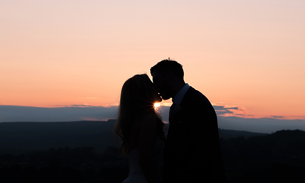 Couple sharing a romantic sunset kiss in silhouette scene