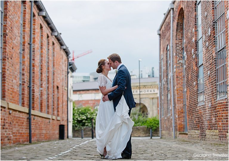 Bride and groom embrace on cobblestone street between buildings