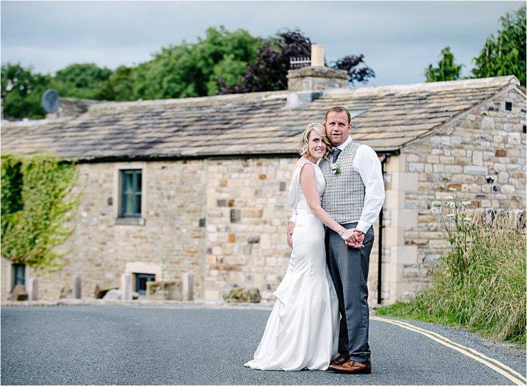 Bride and groom posing together in front of stone cottage