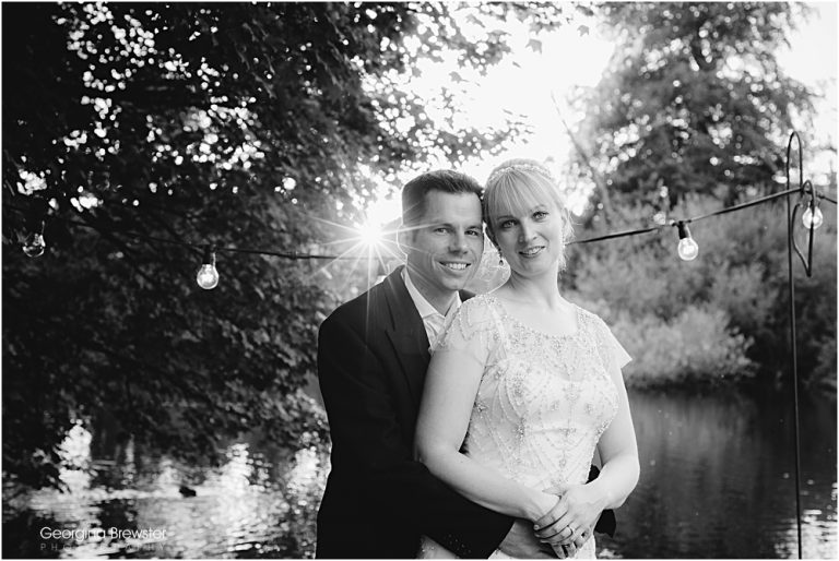 Couple posing by riverside with sunlight in the background