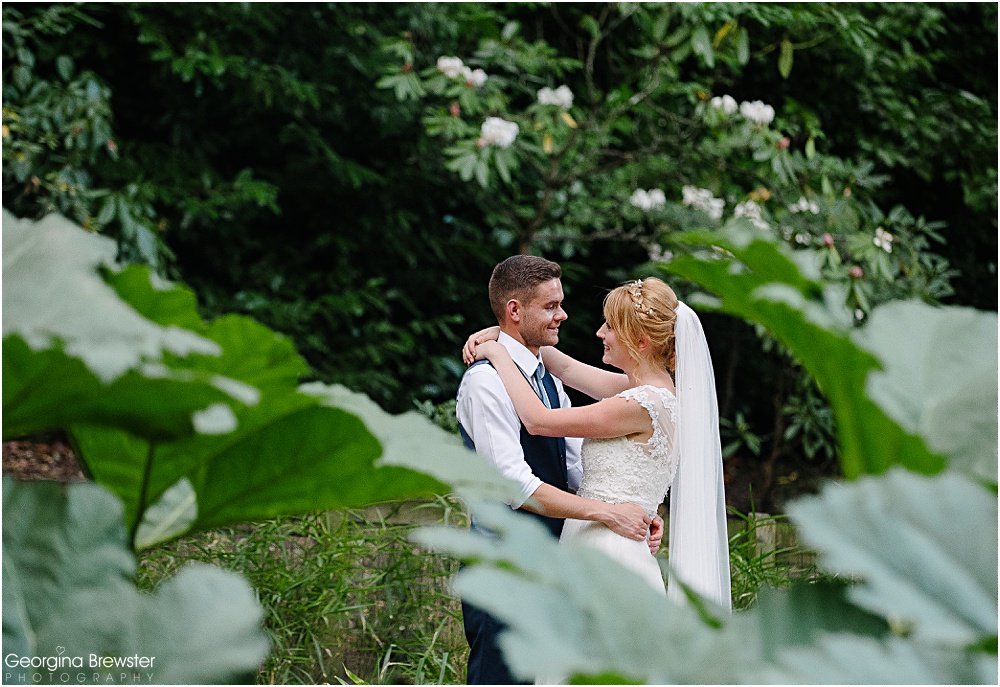 Bride and groom embrace in lush green garden setting
