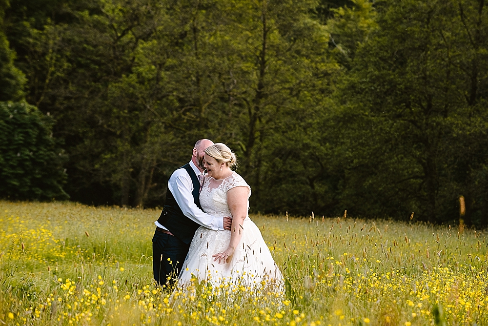 Bride and groom embrace in a lush green meadow landscape