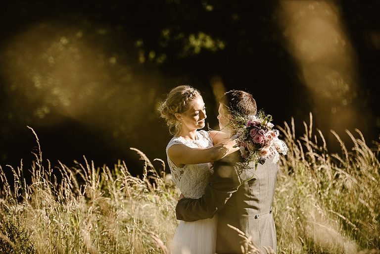 Bride and groom embracing in a sunlit meadow scene
