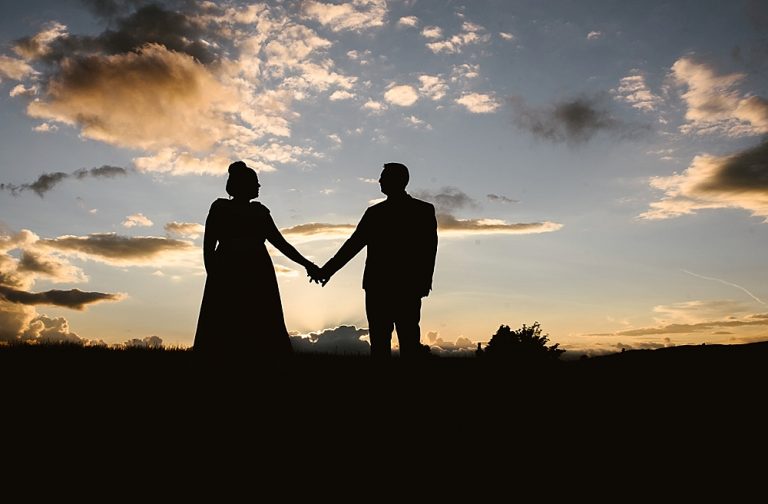 Silhouette of a couple holding hands at sunset on a hilltop