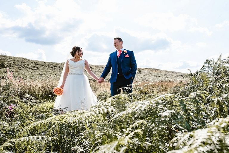 Bride and groom holding hands in countryside landscape