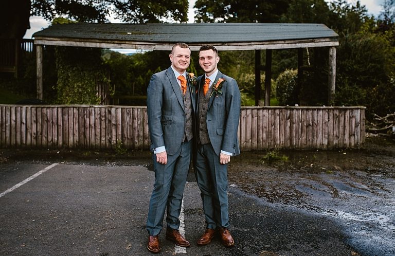 Two men smiling in suits at an outdoor wedding venue