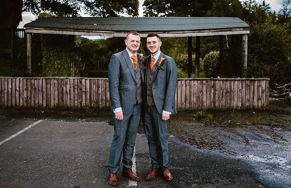 Two men smiling in suits at an outdoor wedding venue