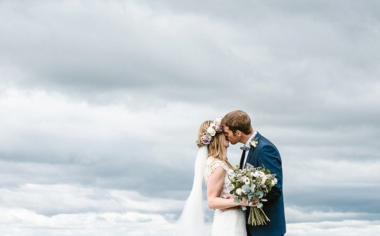 Bride and groom kissing under cloudy sky on wedding day