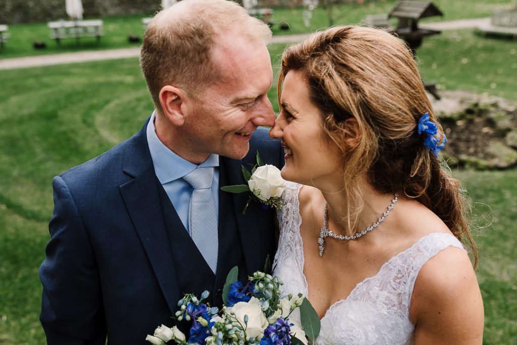 Smiling couple on wedding day with bouquet and greenery