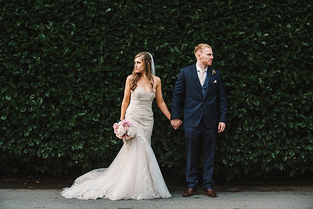 Bride and groom posing in front of green leafy background
