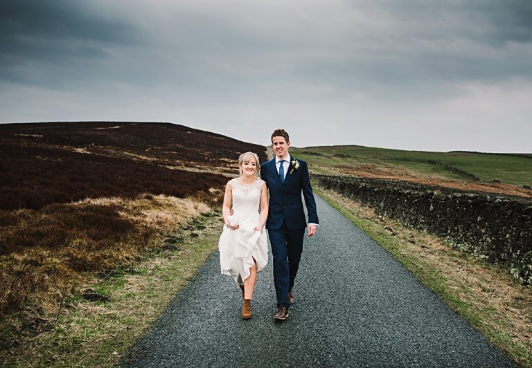 Bride and groom walking on country road under cloudy sky