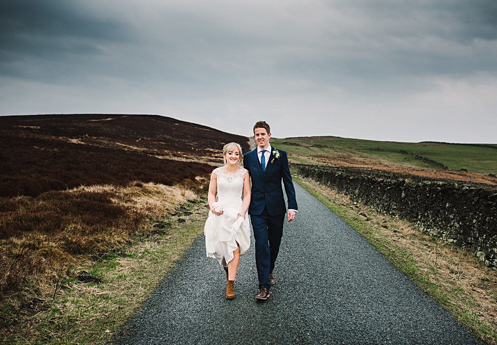 Bride and groom walking on country road under cloudy sky