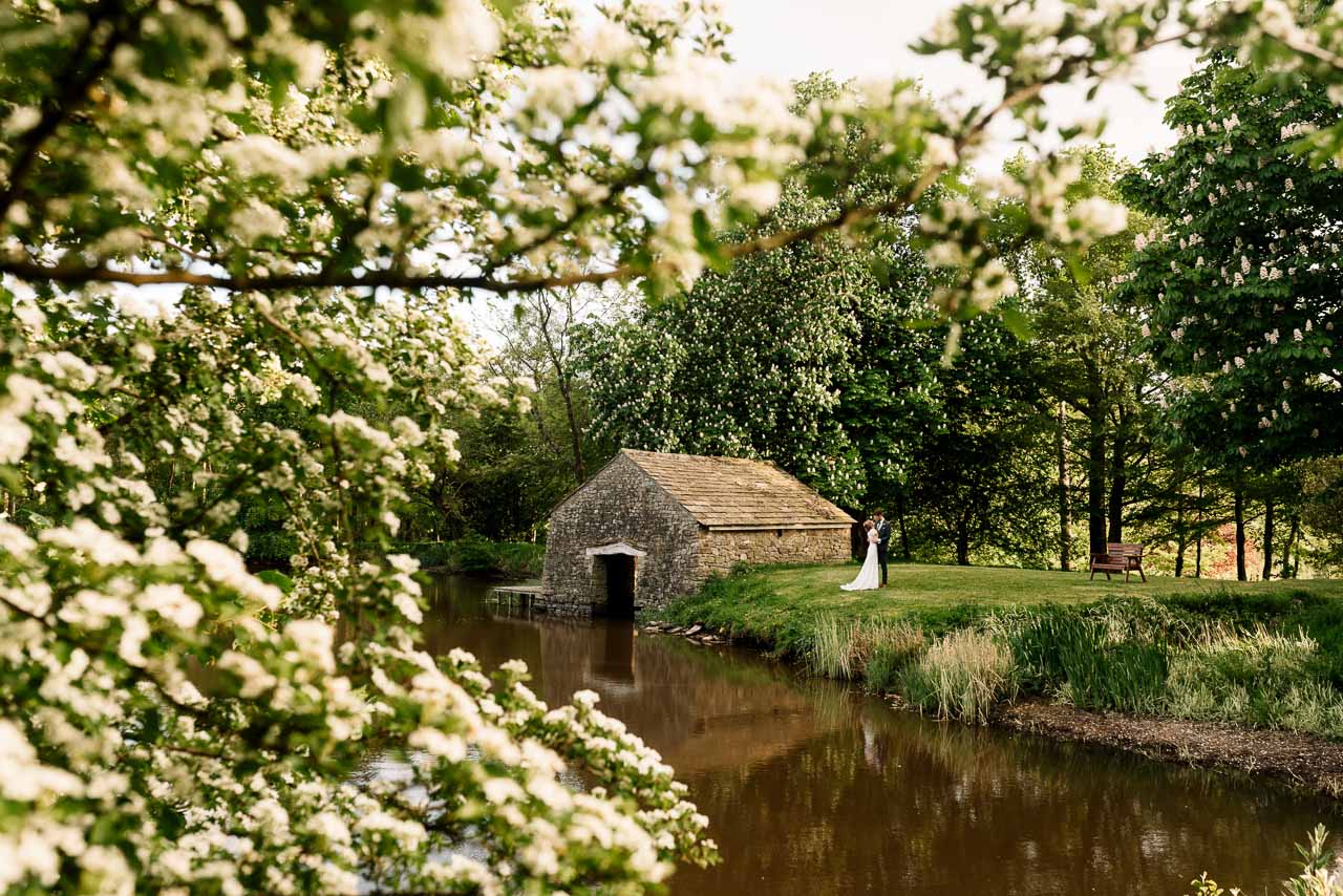 Bride and groom by a rustic stone building near a pond