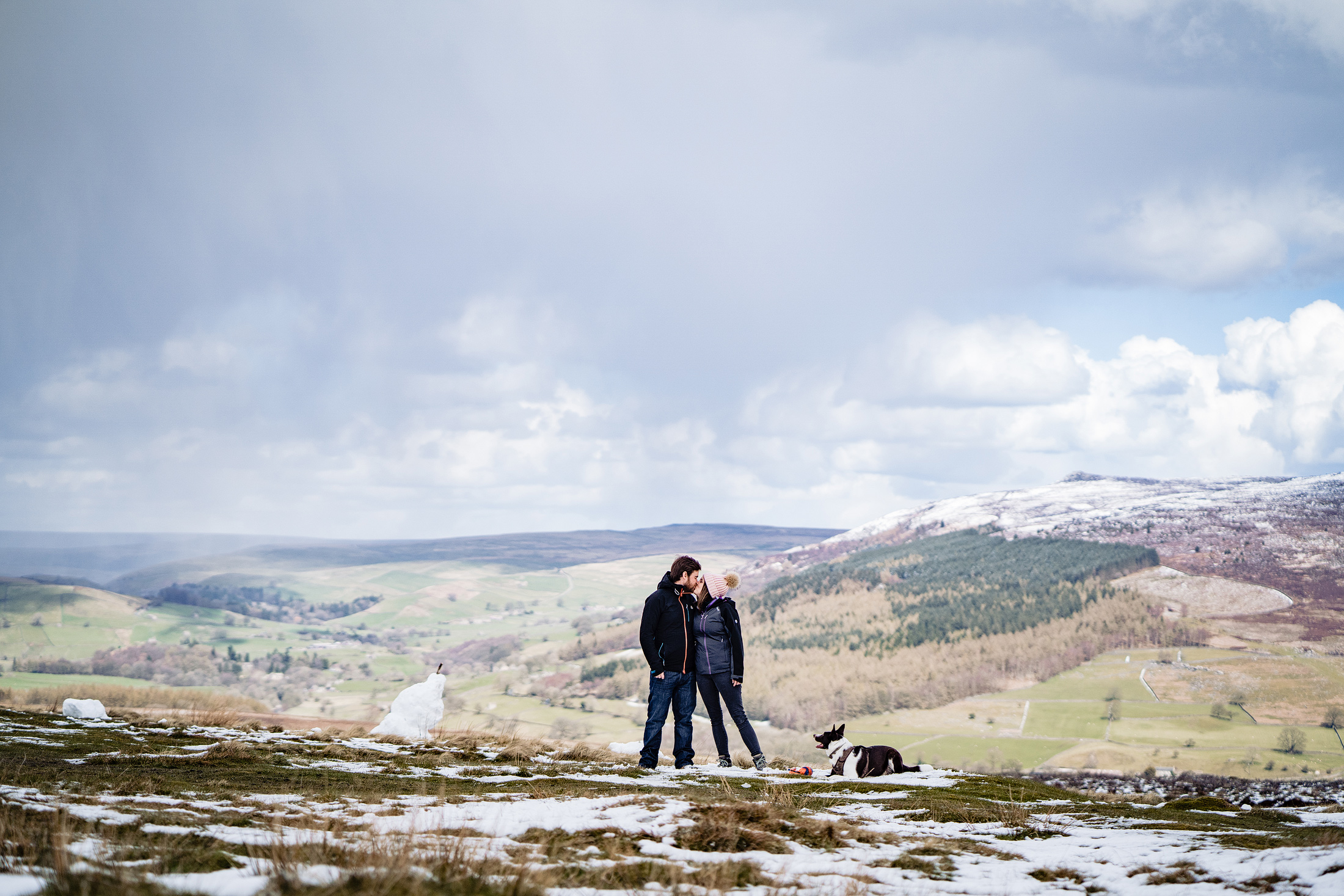 Couple with dog standing on snowy hilltop landscape