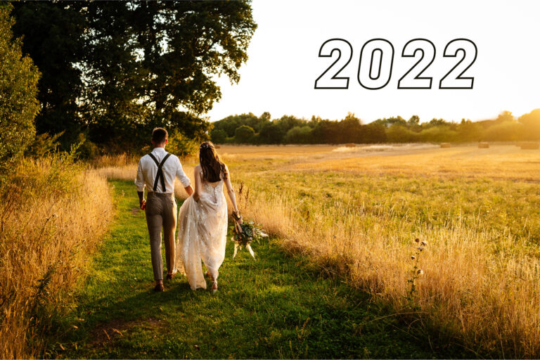 Couple walking in sunlit field at sunset 2022 wedding theme