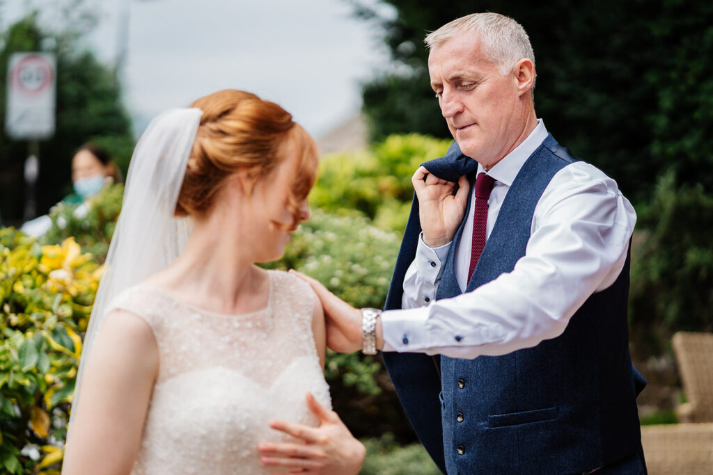 Father adjusts bride's dress on wedding day in garden setting