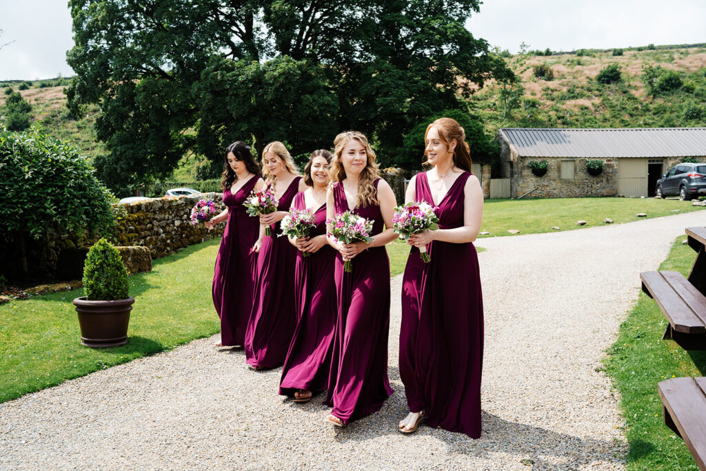 Bridesmaids in purple dresses walking outdoors with bouquets at The Priests House in Barden, North Yorkshire