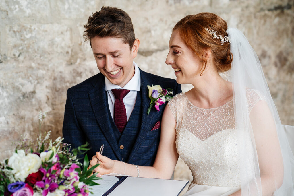 Bride and groom signing wedding register with joyful smiles The Priests House in Barden, North Yorkshire