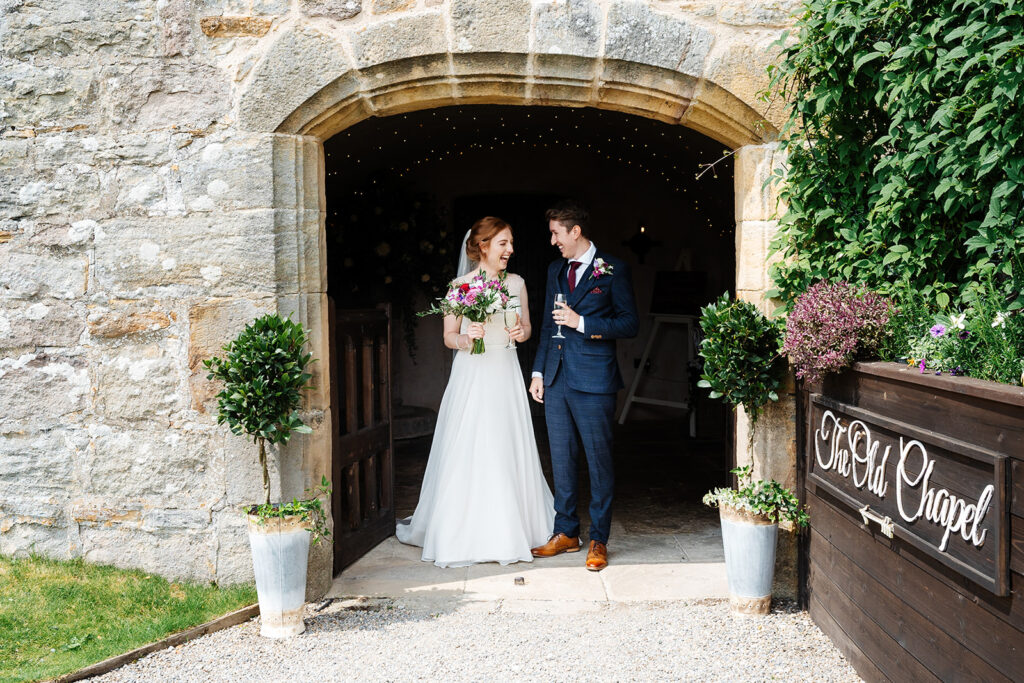 Bride and groom exiting charming rustic stone chapel The Priests House in Barden, North Yorkshire