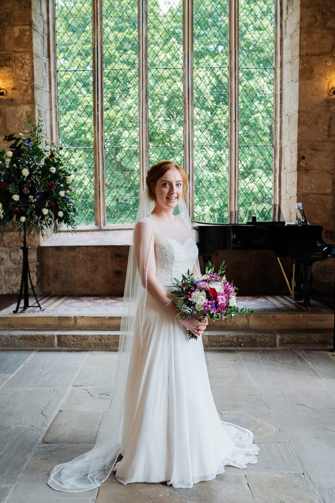 Bride in white gown holding bouquet in elegant stone hall The Priests House in Barden, North Yorkshire