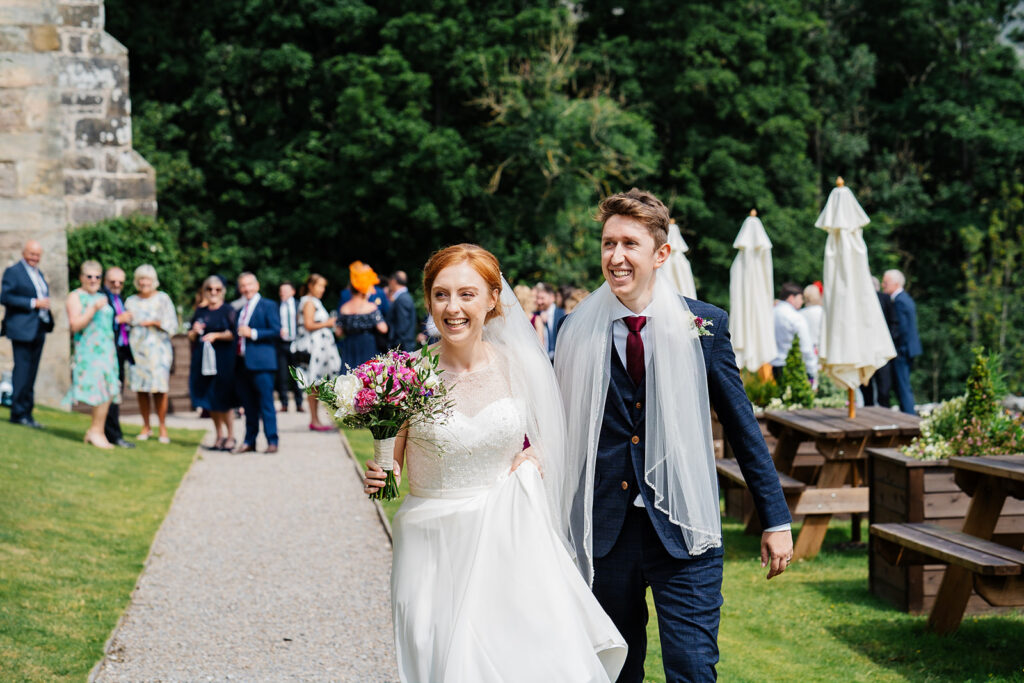Bride and groom walking joyfully at outdoor wedding reception The Priests House in Barden, North Yorkshire