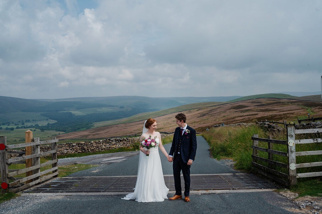 Bride and groom holding hands with scenic hillside backdrop