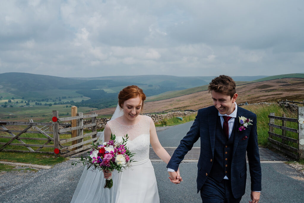 Bride and groom holding hands walking in scenic countryside