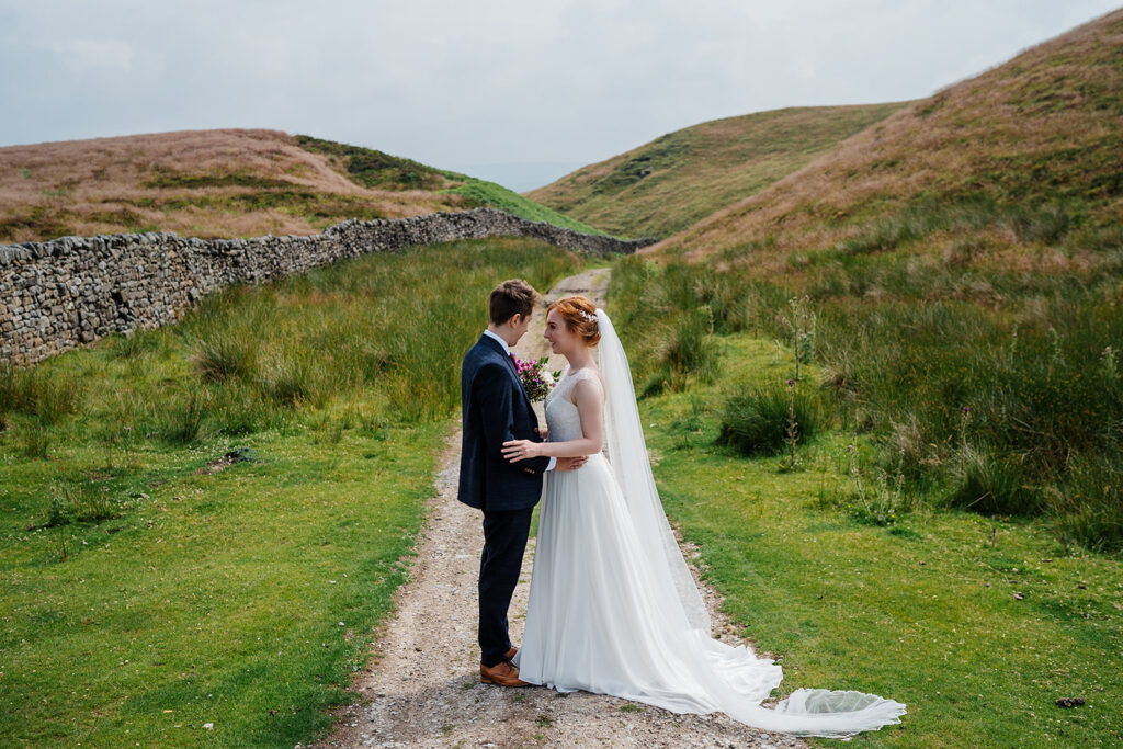 Bride and groom stand in countryside on wedding day