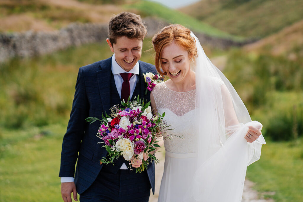 Bride and groom walking happily in countryside with bouquet