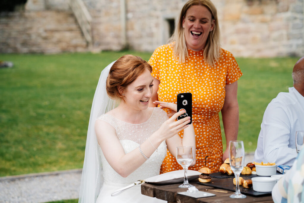 Bride taking a photo at outdoor wedding reception with friend