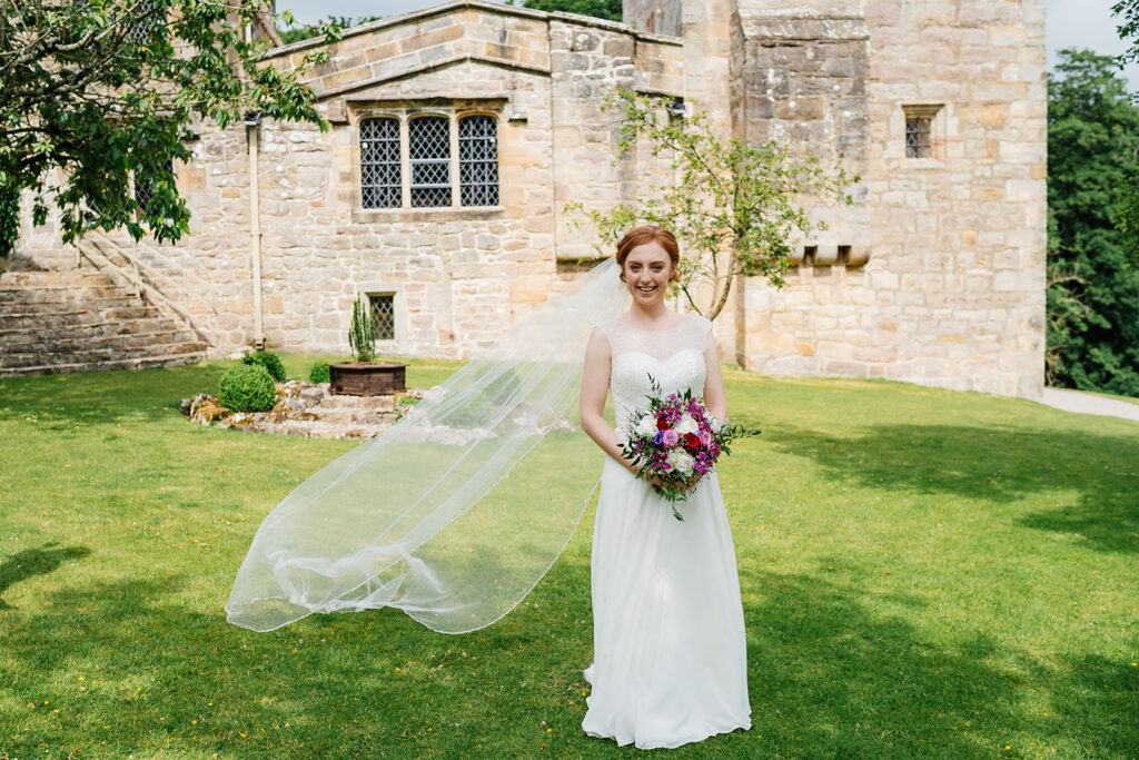Bride in flowing gown holding bouquet near historic stone building