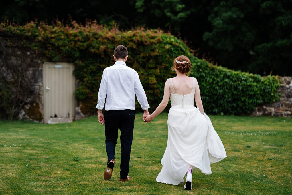 Bride and groom walking hand in hand on grass lawn