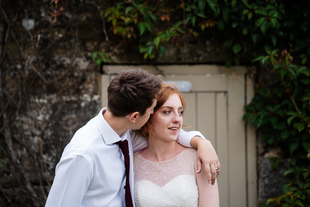 Bride and groom embracing by rustic door in garden setting The Priests House in Barden, North Yorkshire