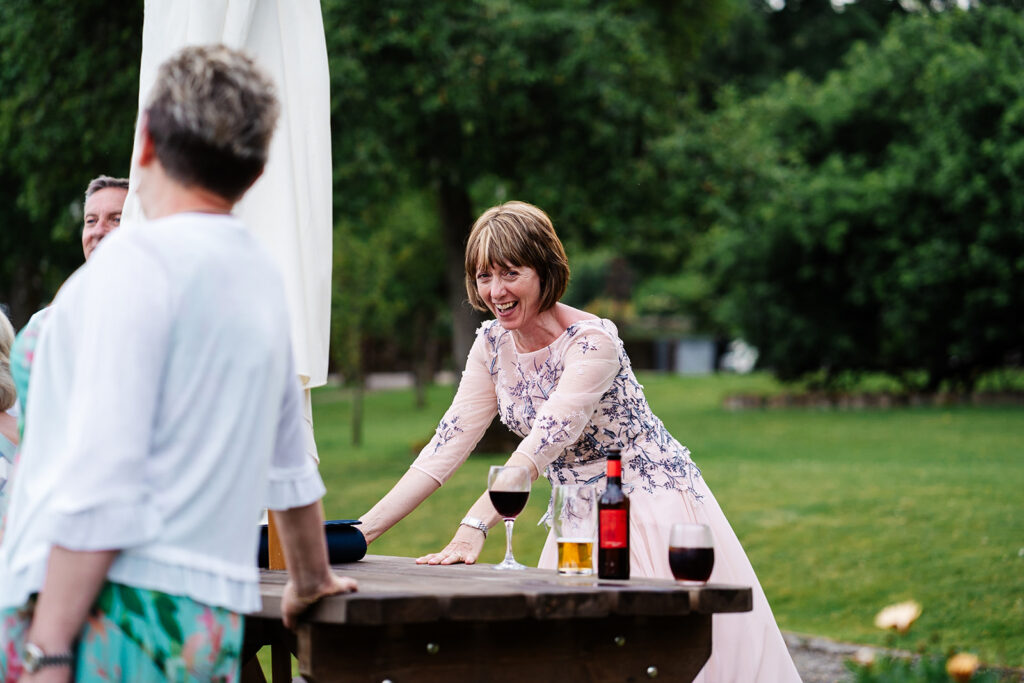 Woman in elegant dress smiling at outdoor gathering with wine.
