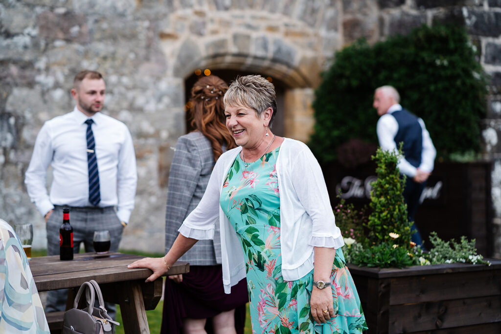Smiling woman in floral dress at outdoor gathering near stone wall