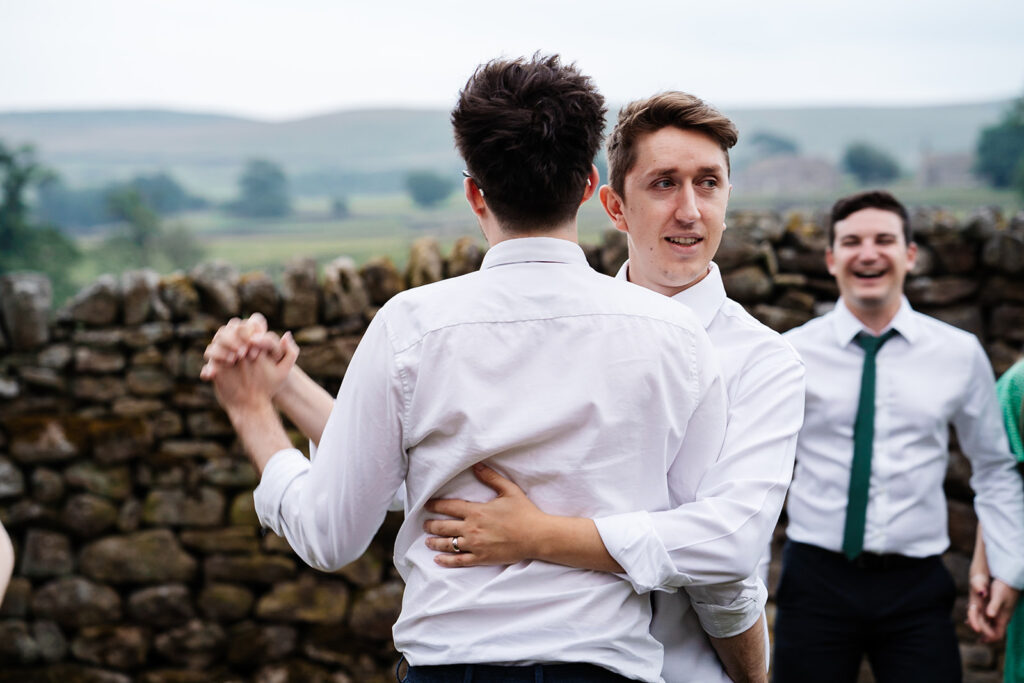 Two friends dancing outside in casual attire near stone wall