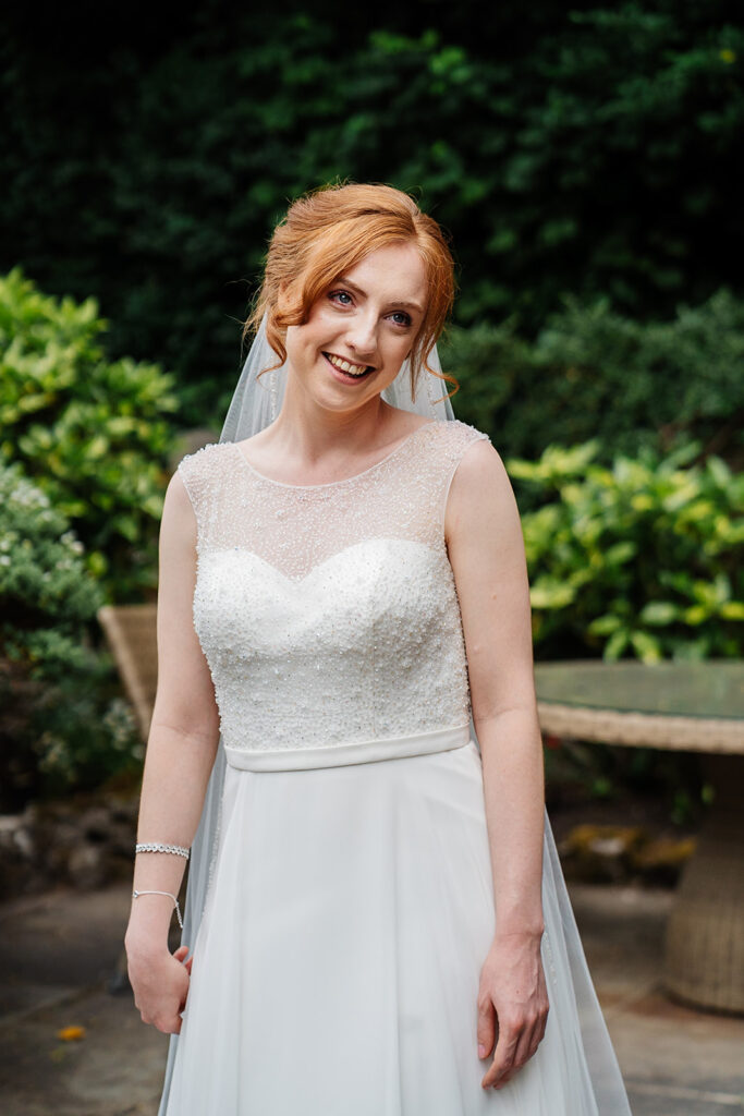 Bride smiling in elegant white dress with garden backdrop