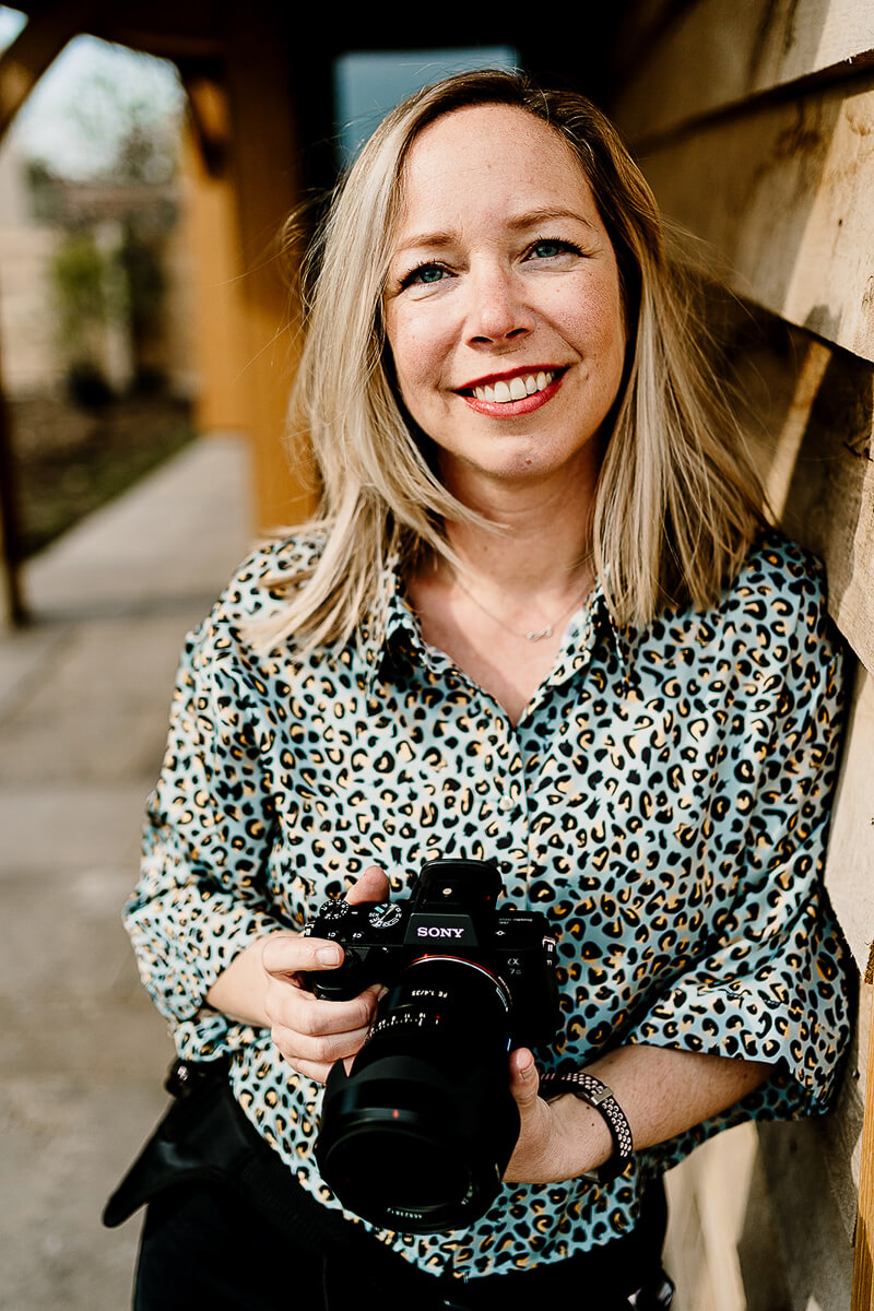 Woman smiling with camera stands outdoors in leopard shirt