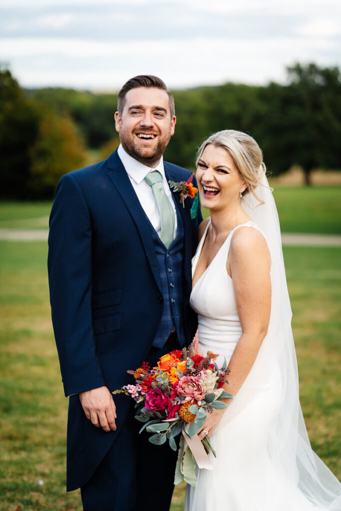Smiling couple in wedding attire holding a colourful bouquet