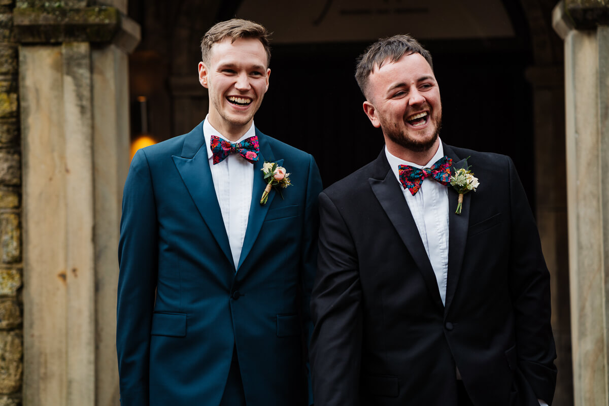 Two grooms happily dressed in suits with floral boutonnieres