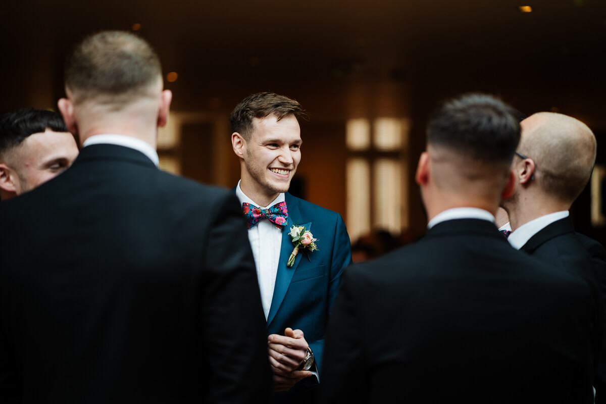 Groom in blue suit chatting with groomsmen at wedding reception