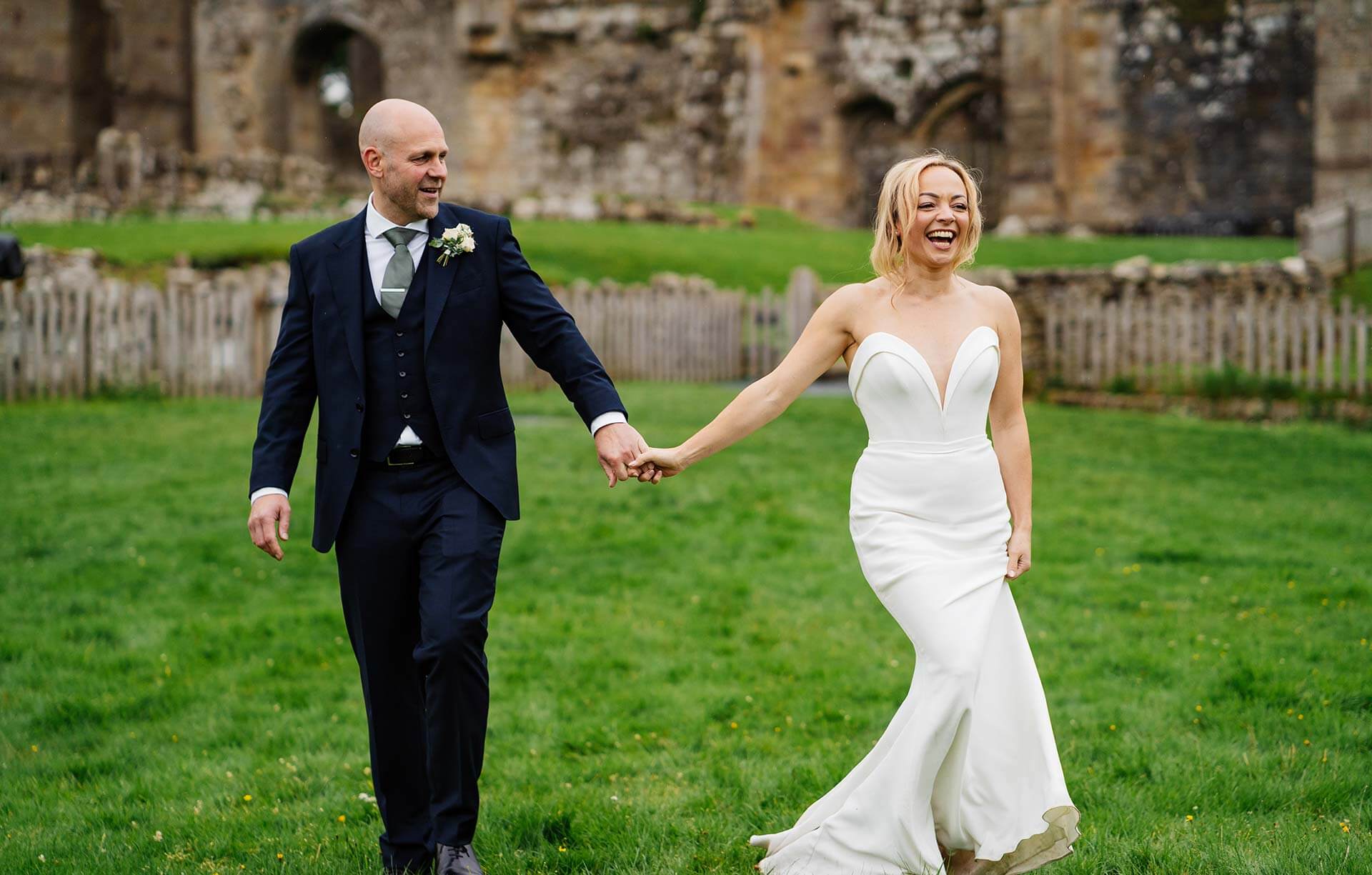 Bride and groom smiling walking in grassy field on wedding day