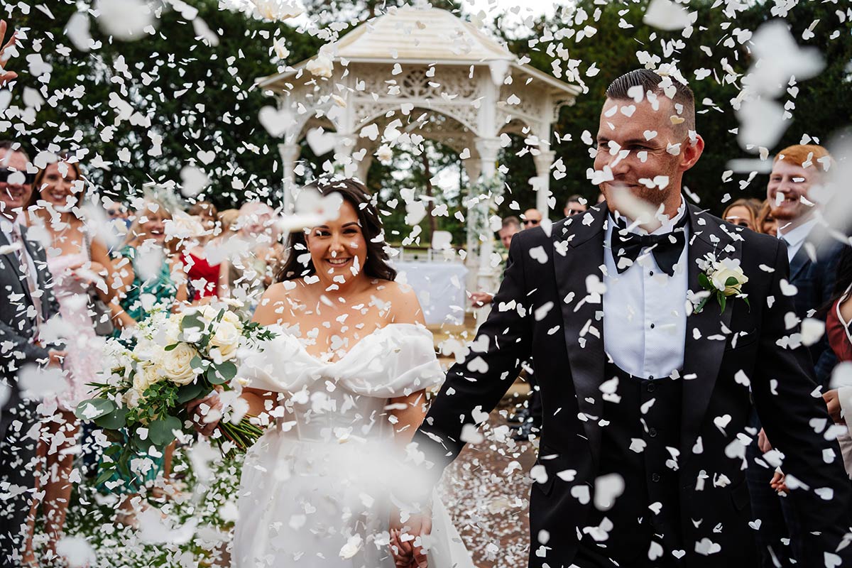 Bride and groom walking through confetti at outdoor wedding