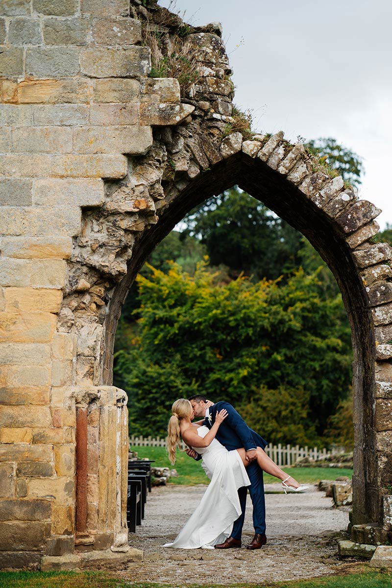 Romantic couple kissing under ancient stone archway in garden