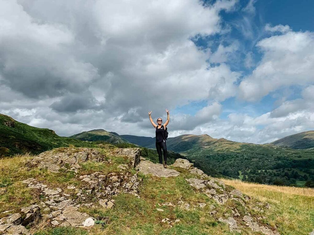 Person celebrating on scenic hilltop with cloudy sky